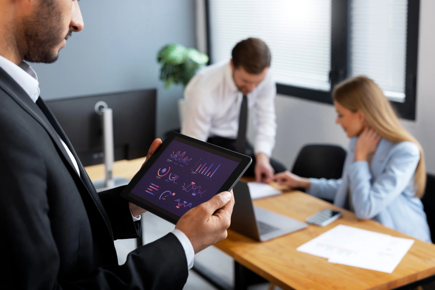 Imagem de destaque: Um home segurando um tablet em uma reunião executiva.